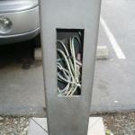 The rectangular hole on the side of this metal light pole is called a 'hand hole' and it should have a metal cover on it. This is dangerous as a child could stick a hand inside and possibly get shocked. This post is located in an apartment complex.